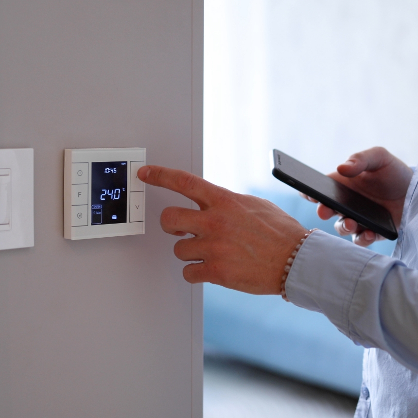 Réglage d’un thermostat connecté mural, smartphone en main