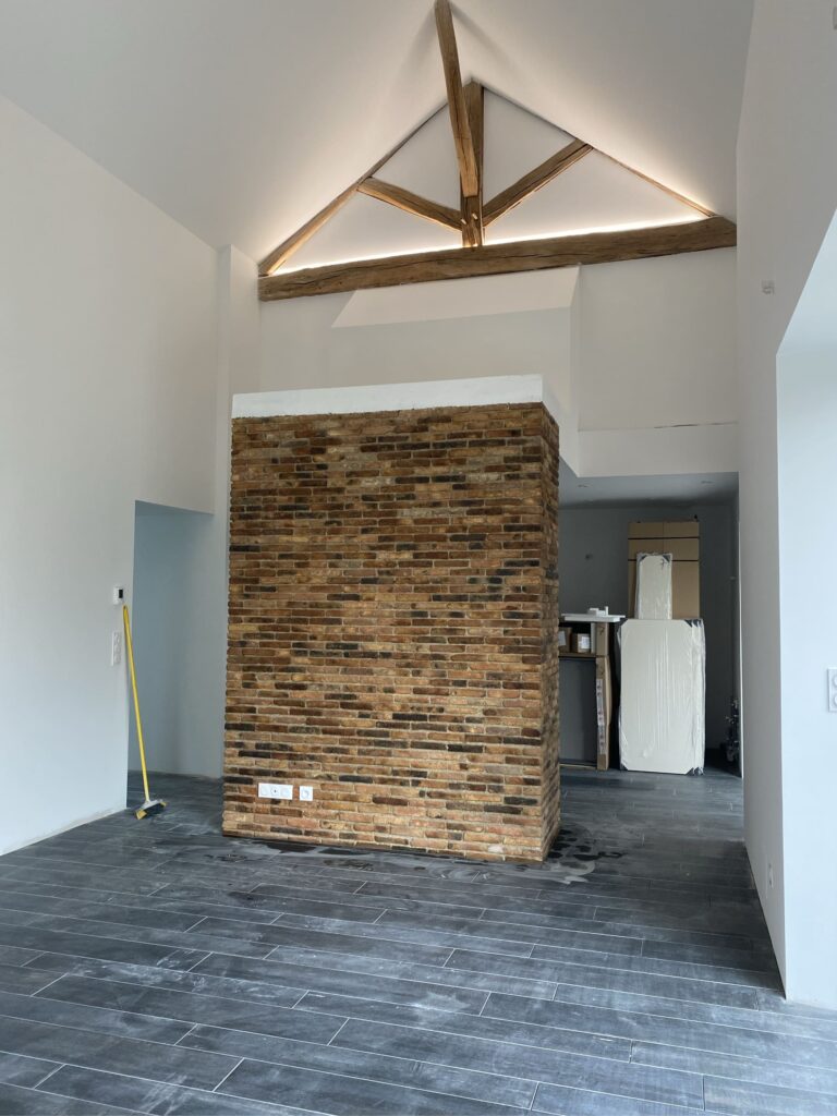 Pièce à vivre en rénovation avec charpente apparente et mur de briques, éclairage indirect