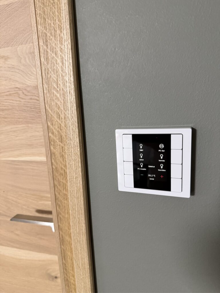 Bouton poussoir KNX à écran intégré posé près d’une porte en bois